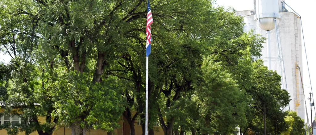 PROMO HIRES Government - Kiowa County Courthouse Eads - Chris Sorensen Flags in front of the Kiowa County Courthouse in Eads, Colorado. The building is surrounded by trees.