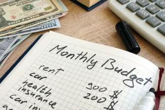 PROMO HIRES Finance - Personal Budget Ledger Calculator Money - iStock - designer491 Notebook open to a page with hand-written "Monthly Budget" at the top. Cash and a calculator are nearby.