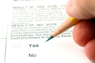 PROMO HIRES - Election - Vote Voting Ballot - Svanblar iStock-146069215 Fingers holding a pencil over an election ballot showing yes and no options