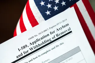 PROMO HIRES Miscellaneous - I-589 Application for Asylum Migrant Immigration - iStock - Eblis Closeup of the corner of a United States Government I-589 immigration form with a United States flag in the background.